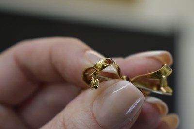 Lot 45 - Yellow metal (750) and red enamel decorated heart-shaped locket on a tied bow brooch fitting